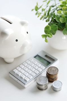 a white piggy bank sitting next to a calculator and some silver coins