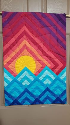 a colorful quilt hanging from the side of a door with an orange sun on it