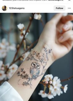 an owl tattoo is on the wrist of a woman with white flowers in front of her