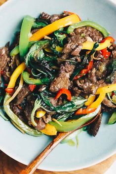 stir fry with beef and vegetables in a blue bowl on a wooden table next to chopsticks