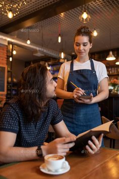 a man and woman sitting at a table in a coffee shop looking at something on the menu