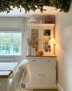 a dining room with white furniture and greenery hanging from the ceiling over it's windows