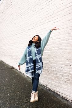 a woman standing in front of a white brick wall with her arms spread out to the side