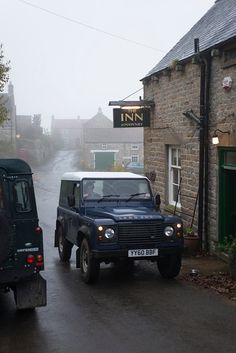 two vehicles driving down the road in front of a brick building on a foggy day