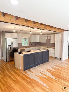 an empty kitchen with wooden floors and white cabinets in the middle, is seen from across the room