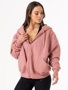 a woman wearing a pink hoodie and black leggings is posing for the camera