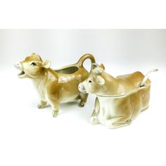 two brown and white cow figurines sitting next to each other on a white surface