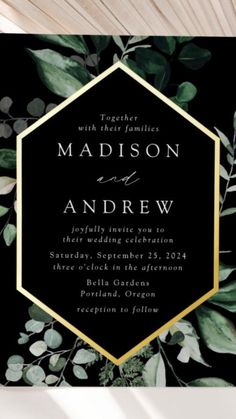 an elegant black and gold wedding card with greenery on the front, featuring a hexagonal frame