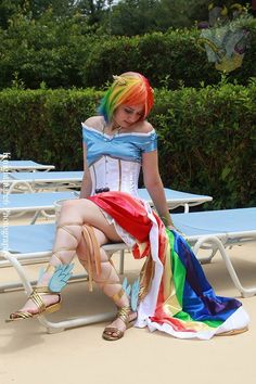 a woman sitting on top of a beach chair wearing a rainbow colored dress and sandals