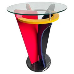 a glass table topped with colorful pieces of art sitting on top of a black pedestal