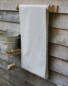 a towel hanging on the side of a wooden wall next to a wire basket and bucket