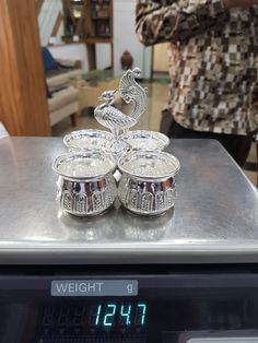 a scale with two silver cups on top of it and a digital clock in the background