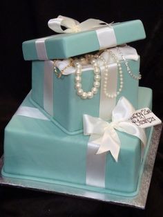 a three tiered cake decorated with pearls and jewelry on top of a blue box