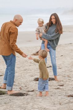 the family is playing on the beach with their little boy and his older sister, who is holding her hand