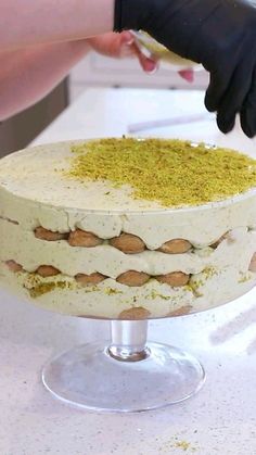 a person in black gloves is decorating a cake with white frosting and yellow sprinkles