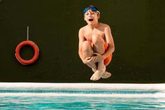 a young boy jumping into a pool with an inflatable life preserver attached to the wall