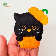 a hand holding a small black cat brooch with an orange flower on its head