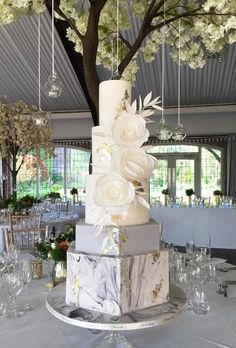 a wedding cake with white flowers on top sits in the middle of a banquet room