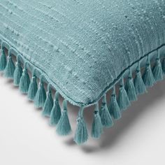 a blue pillow with tassels on the bottom and fringed edges, sitting on top of a white surface