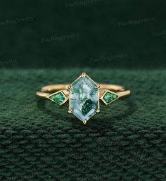 a gold ring with green stones and diamonds on the front, sitting on a green surface