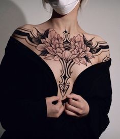 a woman with a mask on her face is wearing a black dress and has flowers tattooed on her chest