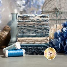 a stack of blue and white quilting material next to two spools of thread