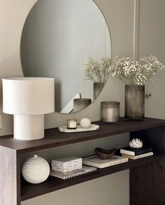 a mirror and some vases with flowers on a shelf next to a table lamp