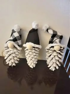 three pine cones with hats on them sitting on top of a black table in front of a white wall