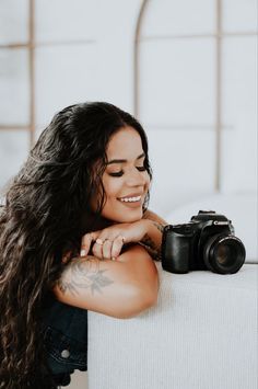 a woman with long hair holding a camera and smiling at the camera while sitting on a couch