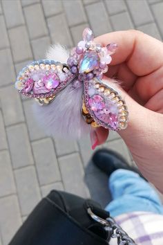 a person is holding a pink and white bow brooch in their left hand on a brick walkway