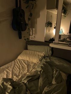 an unmade bed with a guitar hanging on the wall next to it and a mirror