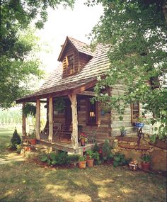 an old log cabin sits in the middle of a yard with potted plants and trees