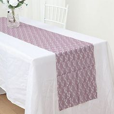 a white table topped with a purple and white table cloth next to a vase filled with flowers