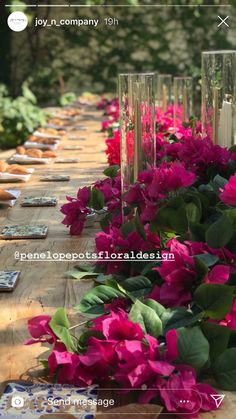 the table is covered with pink flowers and green leaves, along with several clear vases on each side