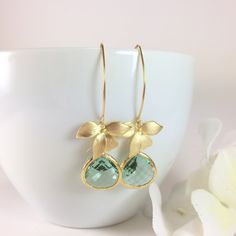 "Aqua Earrings, Aqua Dangle Earrings, Aqua Drop Earrings, Aquamarine Earrings, Gold Earrings, Gold Flower Earrings, Blue Earrings, Orchid Earrings, Wedding Earrings, Bridesmaid Gift, Floral Earrings, March Birthstone, Long Dangle Aqua Blue Earrings Oh so feminine, these earrings are composed of a matte gold orchid flower charm with a sparkly aqua blue faceted glass bezel set teardrop dangling beneath. Simply hung from long gold tone copper ear wires. These earrings are perfect for the bride and Green Flower Earrings With Ear Wire For Wedding, Green Flower Earrings For Wedding With Ear Wire, Gold Flower Earrings, Orchid Earrings, Bridesmaid Necklace Gift, Gold Orchid, Pearl Lariat Necklace, Aqua Earrings, Aquamarine Earrings