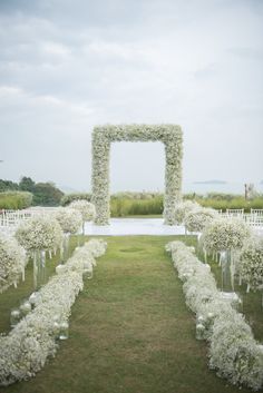 an outdoor ceremony with white flowers and greenery in vases on either side of the aisle