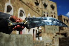 a person holding a large knife in front of an old building with windows and doors