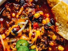 a white bowl filled with chili and corn next to tortilla chips on top of a table