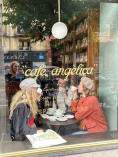 two women sitting at a table in front of a window with coffee cups and saucers