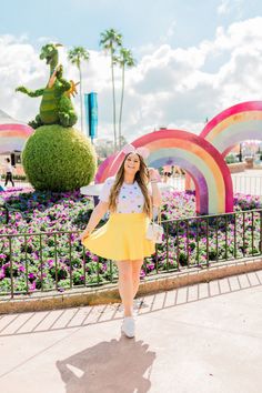 a woman standing in front of a flower garden with a rainbow - shaped sculpture behind her