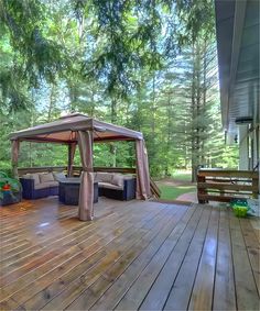 a wooden deck with a gazebo and couches in the middle, surrounded by trees