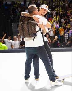 two men hugging each other while standing on a skateboard in front of an audience