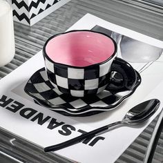 a black and white checkered coffee cup on a plate next to a glass of milk