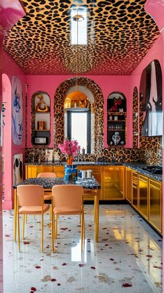 a pink kitchen with leopard print on the ceiling and gold chairs in front of it