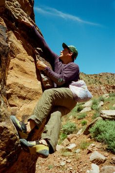 a man climbing up the side of a mountain with his feet on a rock while holding onto a bag