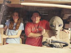 three people standing in the back of a truck with an alien head on it's steering wheel