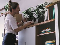 a woman standing in front of a bookshelf holding a box with plants on it