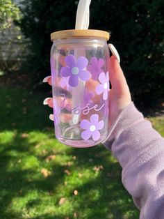 a person holding a mason jar with flowers painted on the lid and straw in their hand