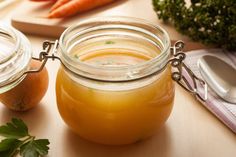 two jars filled with liquid sitting on top of a table next to carrots and broccoli