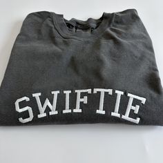 "My absolute favorite tee! Wear it loud and proud; this comfort colors \"SWIFTIE\" tee can be customized with your fave thread color.  Please wash on gentle cycle and dry on low.  If you are wanting a different design, wording, or a different clothing style, please send me a message so we can discuss the details. Please include thread color at checkout" Soft-washed Cotton Crew T-shirt, Cotton Crew T-shirt With Embroidered Graphics, Gray Cotton T-shirt With School Spirit, Collegiate Cotton T-shirt With Embroidered Graphics, Collegiate Embroidered Crew Neck T-shirts, Cotton Tops With Embroidered Graphics For Sports Events, Cotton College T-shirt With Embroidered Graphics, School Spirit Crew Neck T-shirt With Letter Print, School Spirit T-shirt With Letter Print And Crew Neck